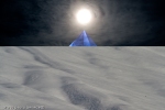 wihte snow and blue pyramid with sun above peak in surreal landscape
